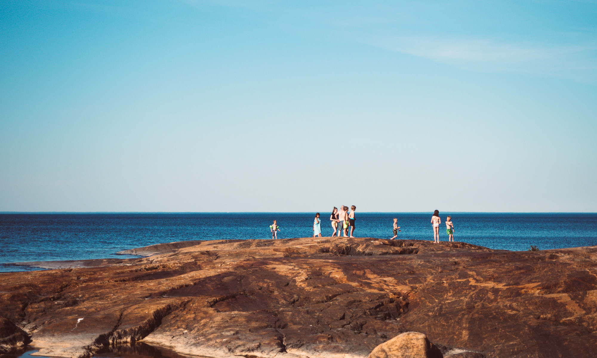 Sommarbild av ett flertal barn på en stor stenhäll vid havet.